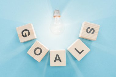 top view of glowing light bulb over 'goals' word made of wooden blocks on blue background, goal setting concept clipart
