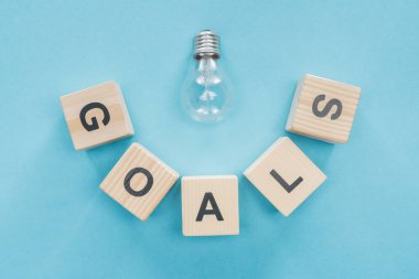 top view of light bulb over 'goals' word made of wooden blocks on blue background, goal setting concept clipart