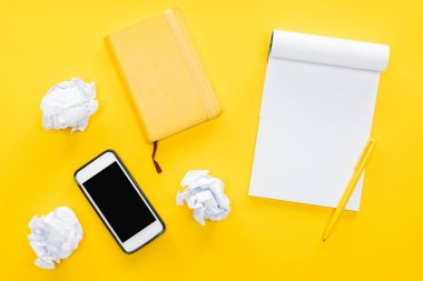 blank notebook, crumbled paper balls and smartphone with blank screen on yellow background clipart