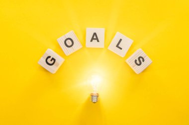 top view of glowing light bulb under 'goals' word made of wooden blocks on yellow background, goal setting concept clipart