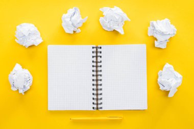 blank spiral notebook and crumbled paper balls on yellow background clipart