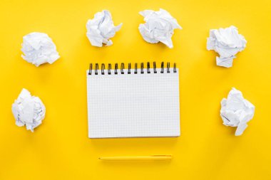 blank spiral notebook and crumbled paper balls on yellow background clipart