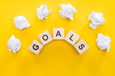 crumbled paper balls over 'goals' word made of wooden blocks on yellow background, goal setting concept clipart