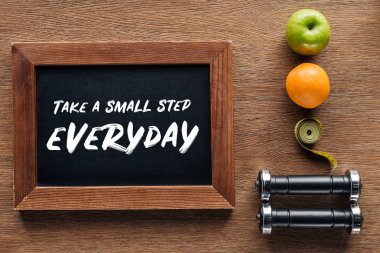 fruits, dumbbells, measuring tape and wooden chalk board with 'take a small step everyday' quote, dieting and healthy lifesyle concept clipart