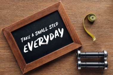 measuring tape, dumbbells and wooden chalk board with 'take a small step everyday' quote, dieting and healthy lifesyle concept clipart