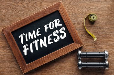 measuring tape, dumbbells and wooden chalk board with 'time for fitness' quote, dieting and healthy lifesyle concept clipart