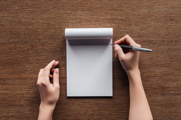 cropped view of person holding pen over blank notebook on wooden background