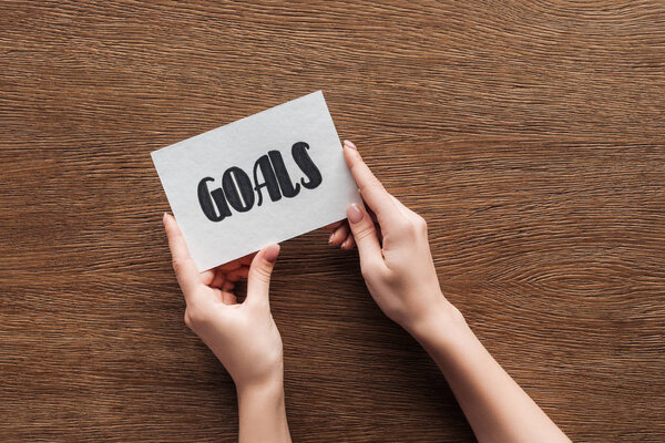cropped view of woman holding card with 'goals' lettering in hands on wooden background