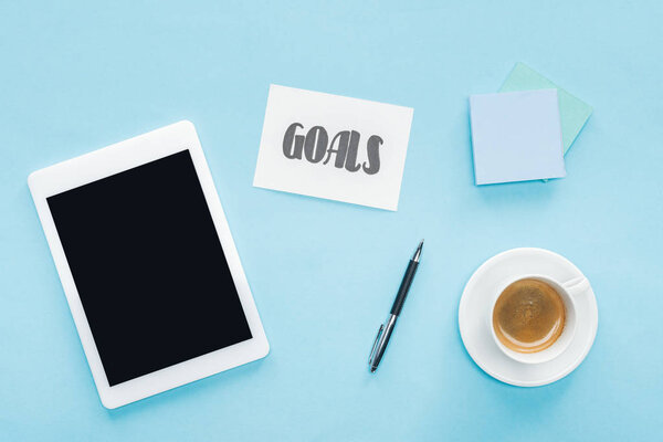 вид сверху цифрового планшета с пустым экраном, надпись "цели" на карточке и липкие ноты на синем фоне
