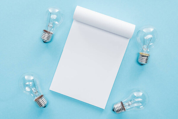 top view of blank notebook with light bulbs on blue background, having idea concept