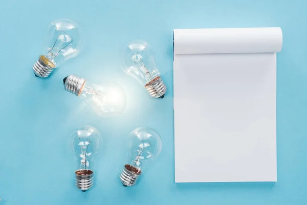 Vista Superior Del Cuaderno Blanco Con Bombillas Sobre Fondo Azul — Foto de Stock