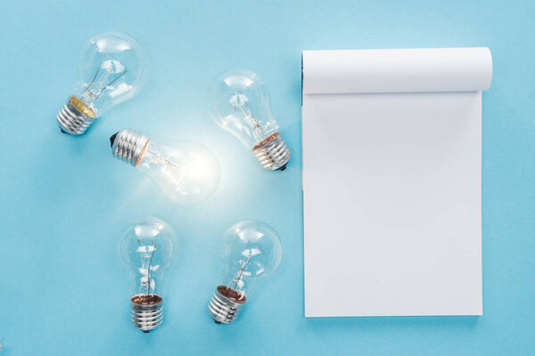 top view of blank notebook with light bulbs on blue background, having new idea concept