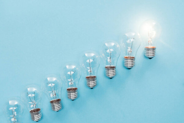 top view of light bulbs in row and one of them glowing on blue background, having new idea concept