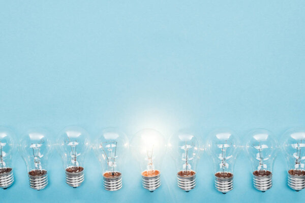 top view of light bulbs in row and one of them glowing on blue background, having new ideas concept