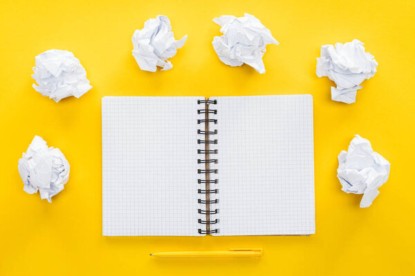 blank spiral notebook and crumbled paper balls on yellow background