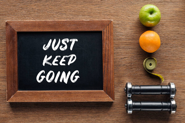 fruits, dumbbells, measuring tape and wooden chalk board with 'just keep going' quote, dieting and healthy lifesyle concept