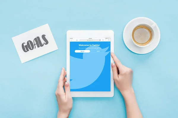 裁剪的女性视图使用数字平板电脑与推特应用程序在屏幕上 目标字母卡和咖啡在蓝色背景 — 图库照片