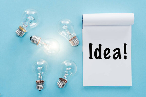 notebook with 'idea' word near light bulbs with glowing one, having new ideas concept