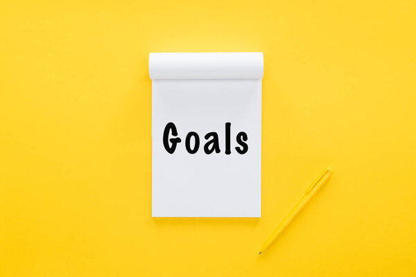 Top view of notebook with 'goals' word on yellow, goal setting concept
