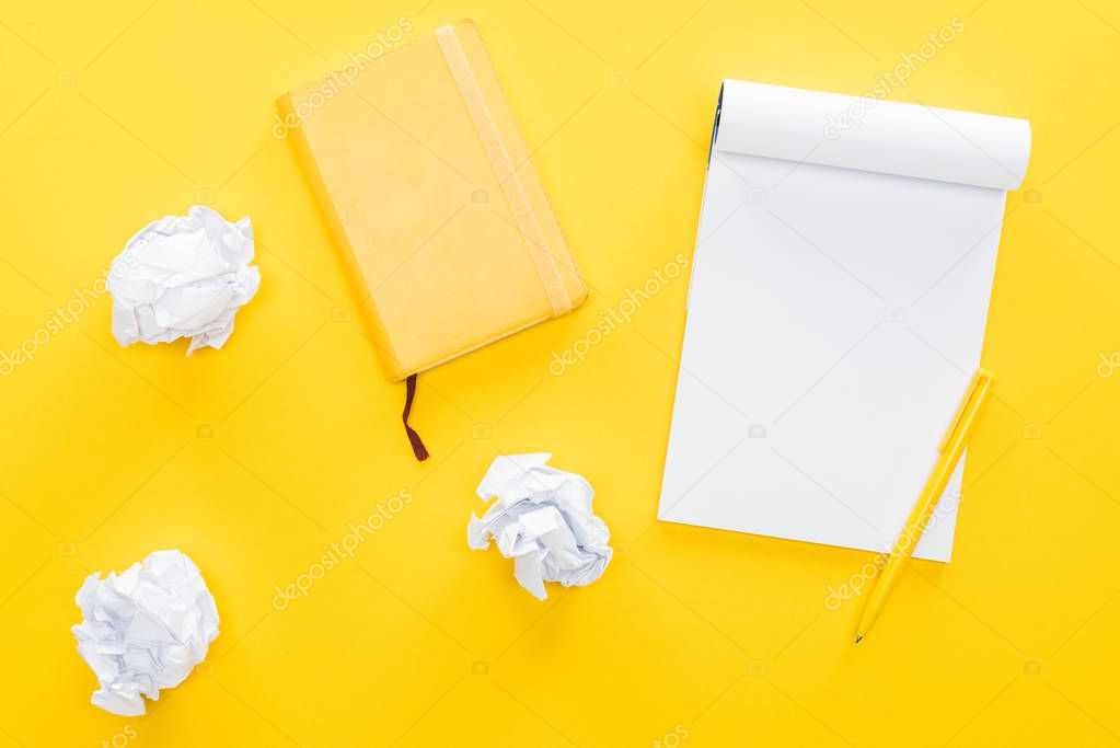 blank notebook and crumbled paper balls on yellow background