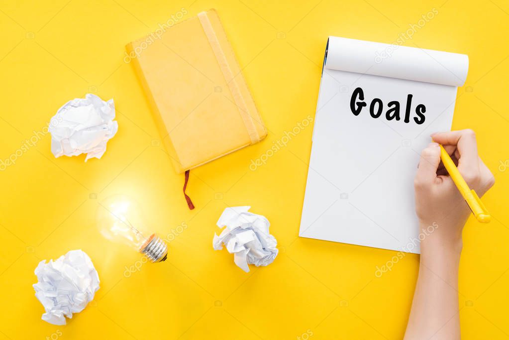 notebook with 'goals' word, crumbled paper balls and glowing light bulb, goal setting concept