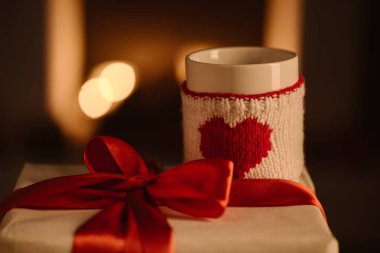  present and knitted mug with heart symbol on blurred background clipart