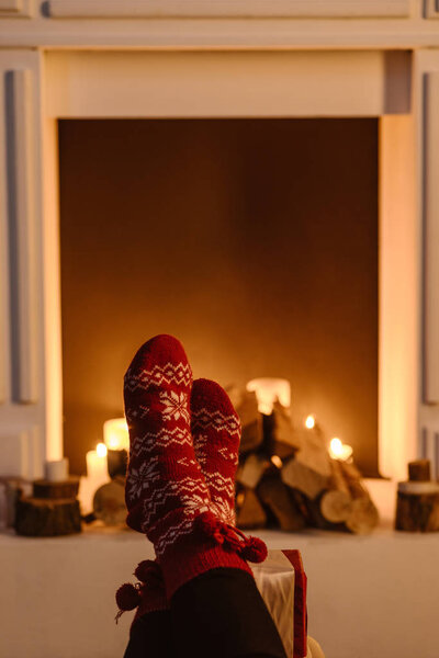 cropped view of woman in festive winter socks with fireplace on background