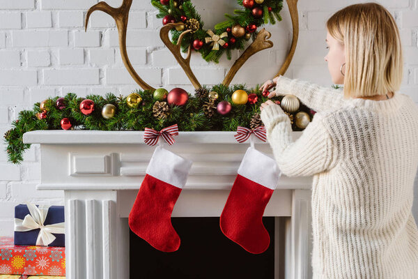 young woman adjusting christmas baubles at fireplace