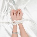 Bovenaanzicht van vrouwelijke handen begrensd met touw met satijn doek op achtergrond