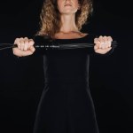 Teilansicht einer Frau mit lederner Peitsche, beide Hände isoliert auf schwarz