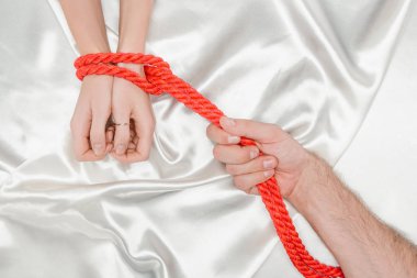 cropped view of male hand bounding female hands with bright red rope clipart