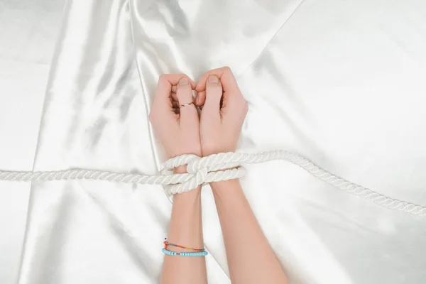 サテンの布の背景をロープで囲まれた女性の手の上から見る  — 無料ストックフォト