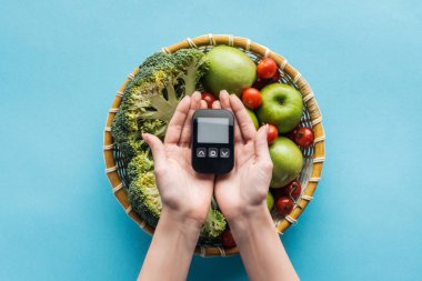 top view of glucometer in female hands with vegetables and apples on blue background clipart