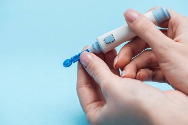 cropped view of woman testing glucose level with disposable needle on blue background clipart