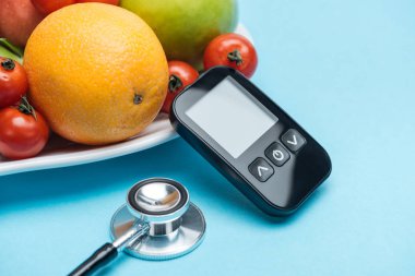 close up view of glucometer and stethoscope with tomatoes and fruits on blue background clipart