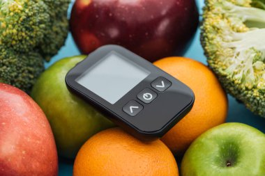 close up view of glucometer among fruits and broccoli on blue background clipart