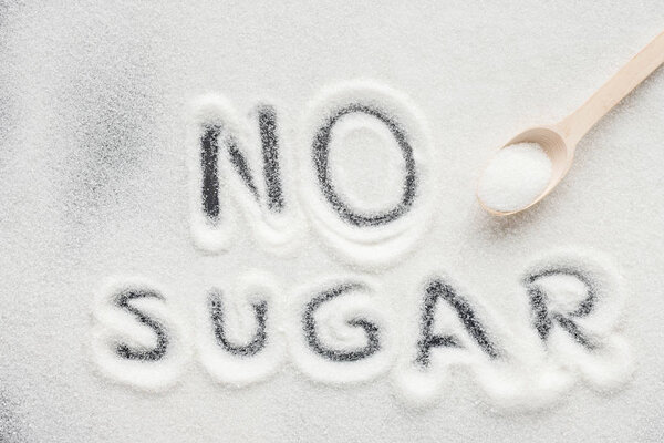 "no sugar" lettering written on granulated sugar with wooden spoon