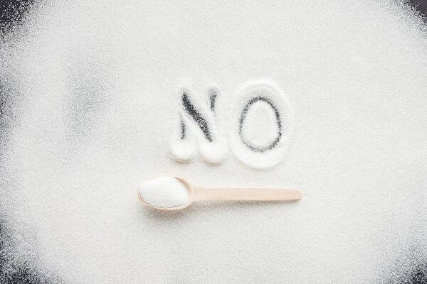 top view of handwritten word "no" on granulated sugar with wooden spoon
