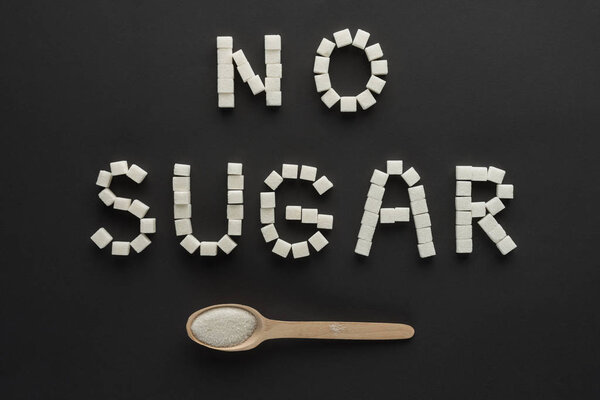 flat lay of "no sugar" lettering made of cubes with wooden spoon isolated on black 