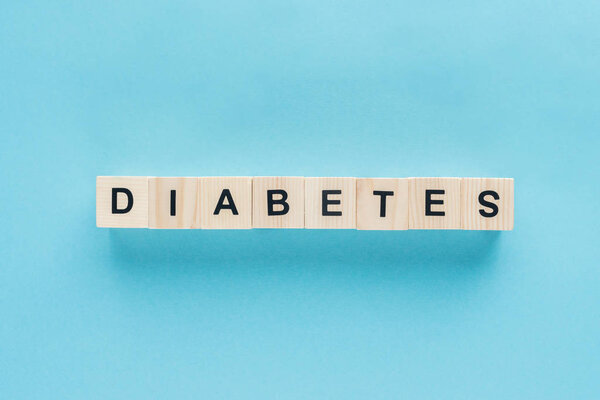 вид сверху на надпись "сахарный диабет" из деревянных кубиков на синем фоне
