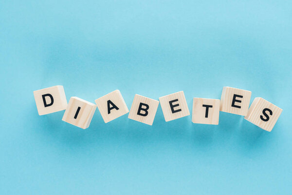 top view of "diabetes" lettering made of wooden cubes in scatter on blue background