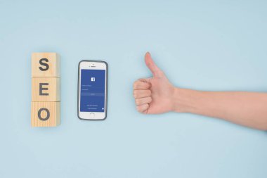 Başparmak yukarıya facebook app ile çevre smartphone üzerinde açık mavi renkli koyarak kadın seo Yöneticisi üstten görünüm 