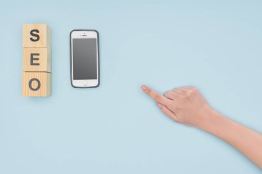 Kadın el smartphone ve küpleri açık mavi renkli seo yazı ile işaret üstten görünüm 