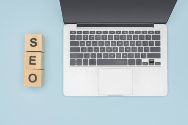 Dizüstü bilgisayar ve tahta küpleri ışık mavi artalanları seo yazı ile üstten görünüm 