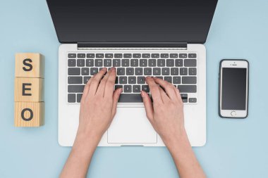Laptop klavye açık mavi renkli Smartphone'da yakınındaki yazarak kadının üstten görünüm 
