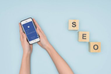 Açık mavi renkli smartphone ile facebook app ahşap küpleri yakın tutan kadın üstten görünüm 