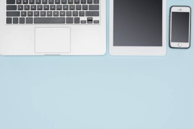 Açık mavi renkli üzerinde laptop, dijital tablet ve smartphone üstten görünüm 