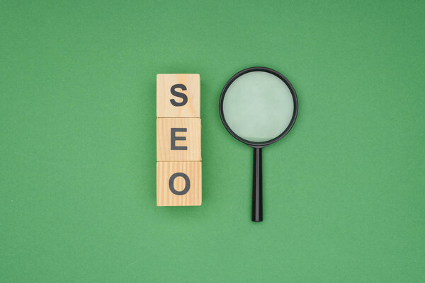 Top view of wooden blocks with letters and magnifier on green background 