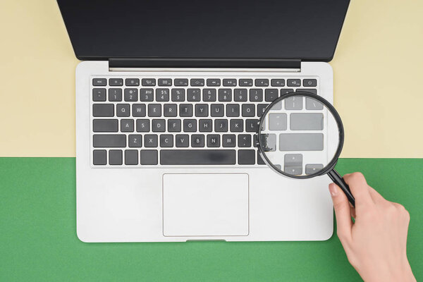 Top view of woman holding magnifier in hand above laptop 