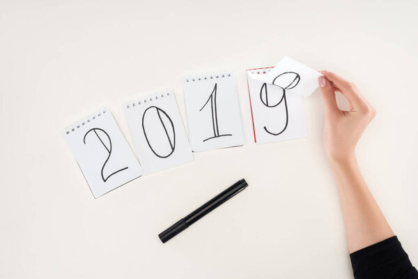 partial view of woman flipping over date written on notes symbolizing change from 2018 to 2019 isolated on white